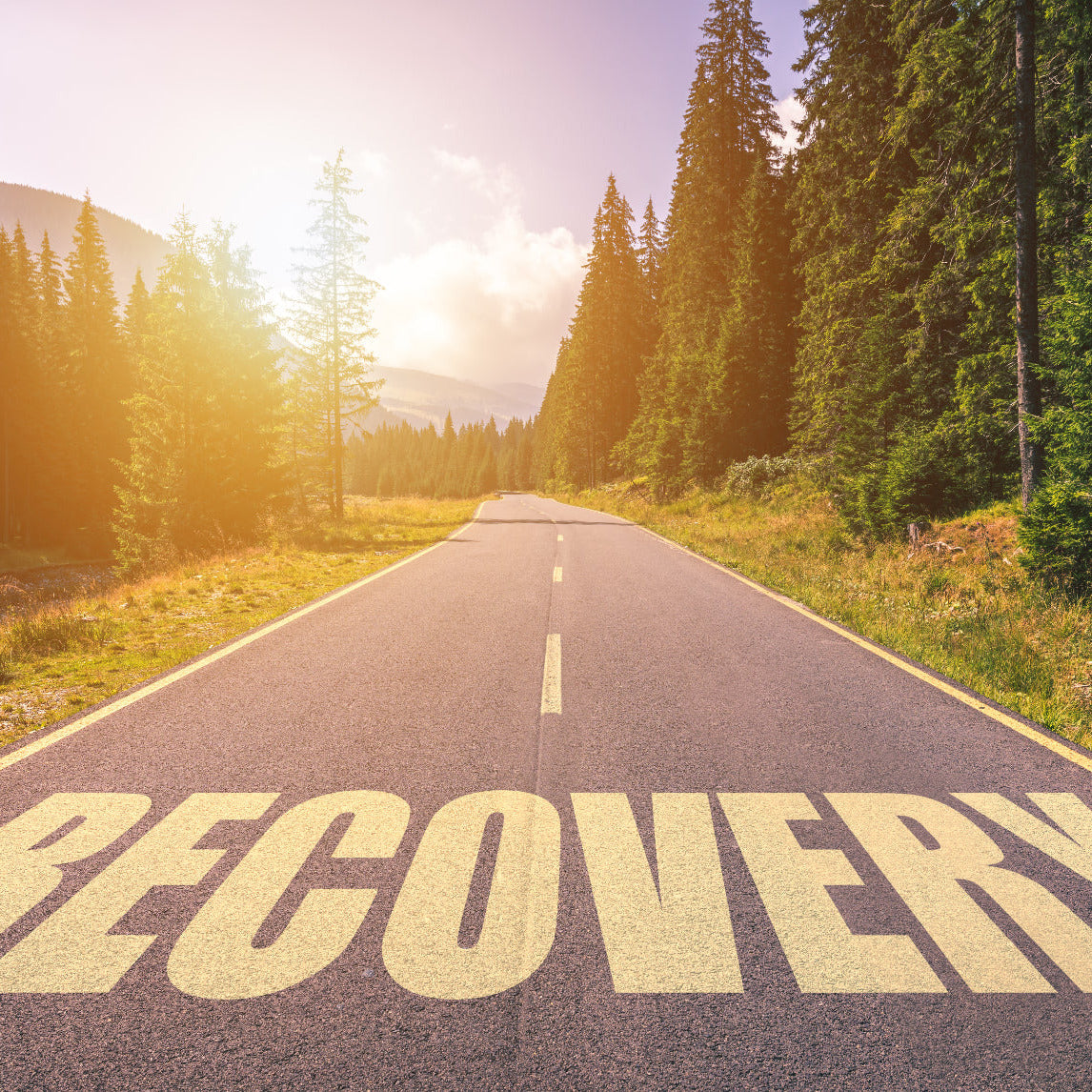 Road with 'RECOVERY' written on it surrounded by trees and sunlit sky