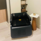 Black massage chair in a room with shelves and a small table.